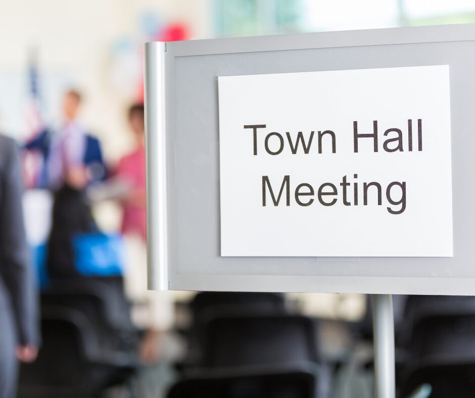 a sign reading Town Hall Meeting with people talking out of focus in the background
