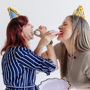 Two women eating cake with their arms linked. These women are Ang and Mel, the directors of spectrum comms